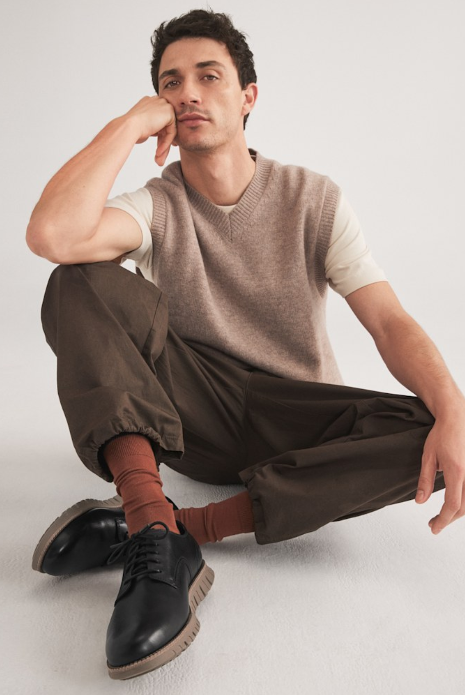 male model in a smart casual outfit sitting on a studio floor while wearing black oxford shoes