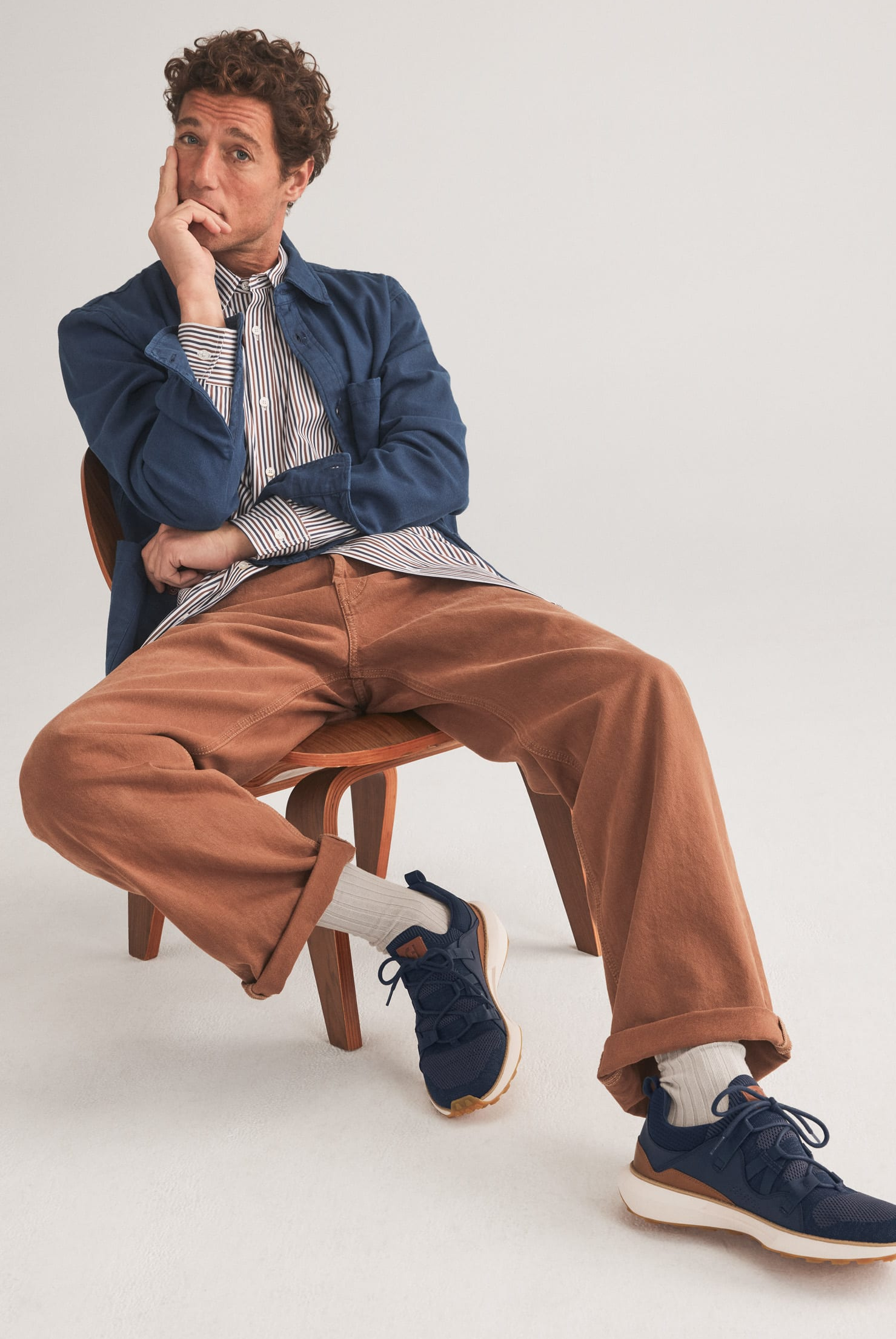 male model sitting on a chair wearing a white button-down top with dark pants and brown loafers