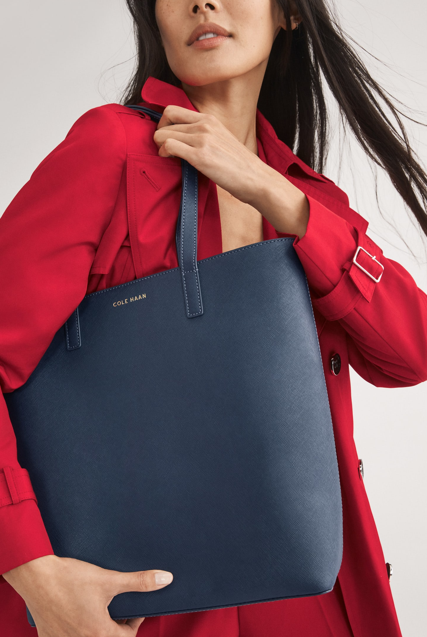 female model wearing a red trench coat with a navy tote bag on her shoulder